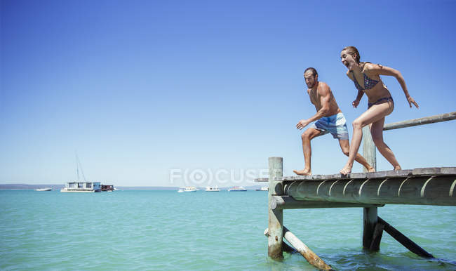 Couple jumping off wooden dock together — Stock Photo