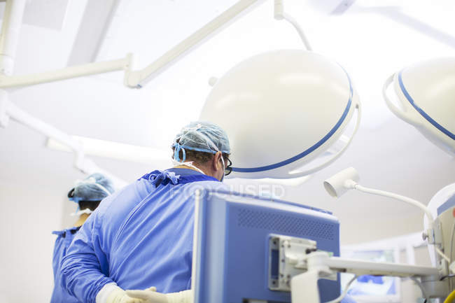 Vue arrière du médecin portant casquette chirurgicale, masque et robe dans le bloc opératoire — Photo de stock