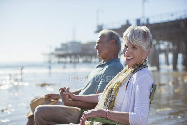 Retrato de casal sênior relaxante em cadeiras de gramado na praia — Fotografia de Stock