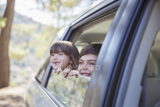 Happy brother and sister looking out car window — Stock Photo