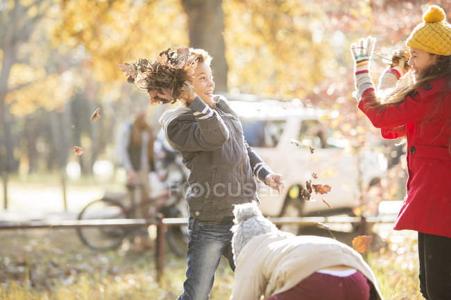 Мальчик бросает осенние листья в девушку в парке — стоковое фото