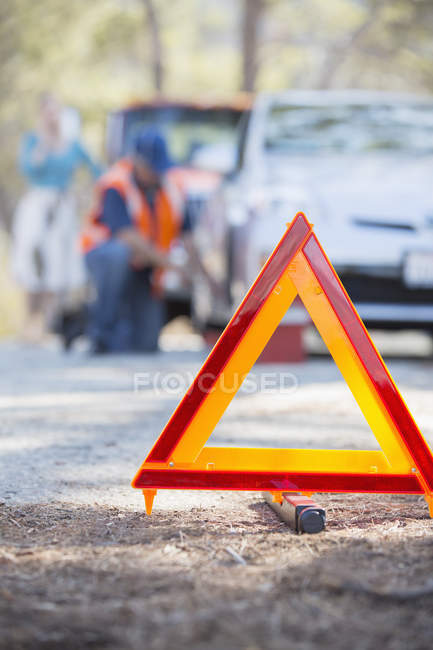 Mecánico de carretera ayudando a la mujer detrás del triángulo de advertencia - foto de stock