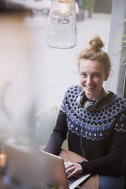 Portrait smiling young woman using laptop in cafe window — Stock Photo