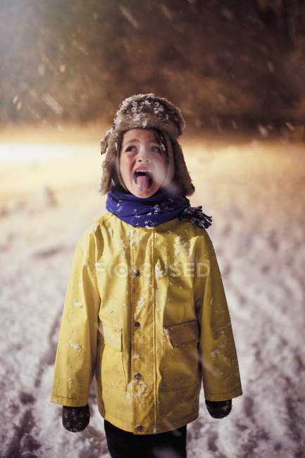 Мальчик в теплой одежде высовывает язык, пробует снег — стоковое фото