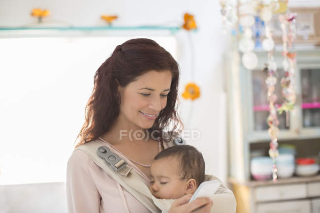 Madre sosteniendo bebé niña en la cocina - foto de stock