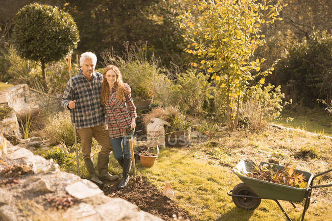 Retrato sonriente pareja jardinería en soleado jardín de otoño - foto de stock