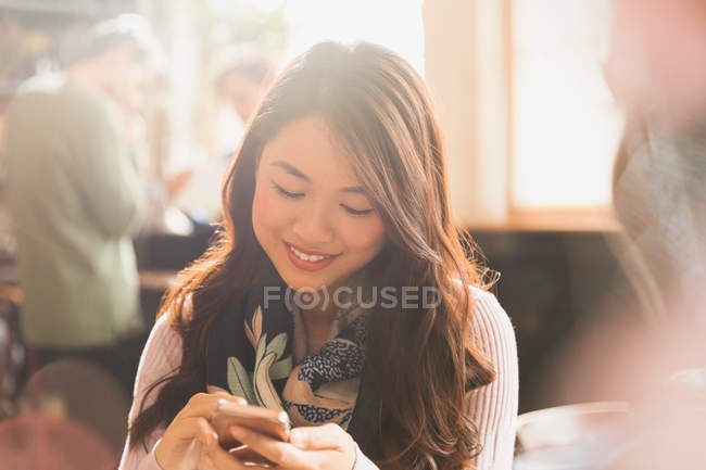 Усміхаючись Китайська жінка текстові повідомлення з мобільного телефону в кафе — стокове фото