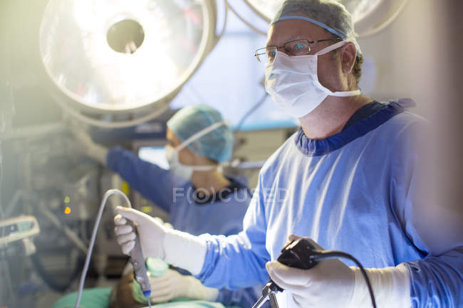 Cirurgião masculino segurando equipamentos de laparoscopia durante cirurgia em sala de operações — Fotografia de Stock