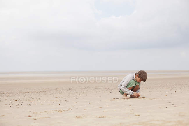 Хлопчик грає в піску на пляжі похмурим літо — стокове фото