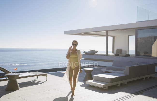 Woman in bathing suit walking on sunny modern, luxury home showcase exterior patio with ocean view — Stock Photo