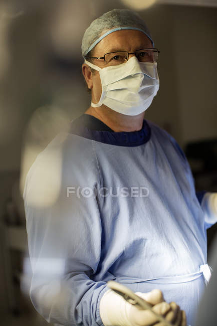 Cirurgião que usa máscara cirúrgica, boné, luvas e vestido na sala de operações — Fotografia de Stock