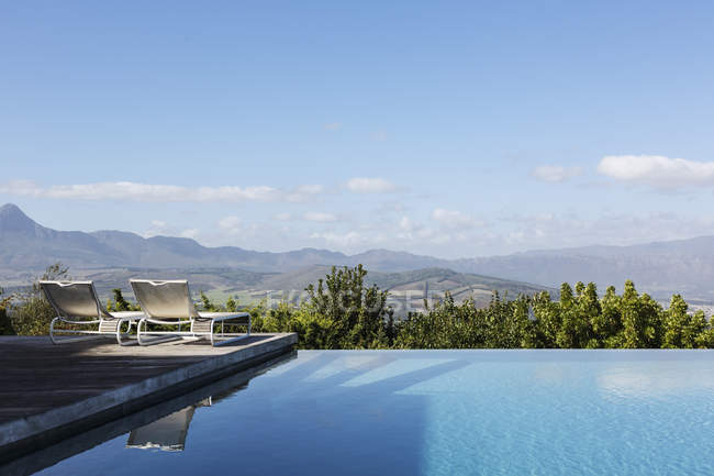 Piscine à débordement de luxe et chaises longues avec vue sur la montagne sous un ciel bleu ensoleillé — Photo de stock