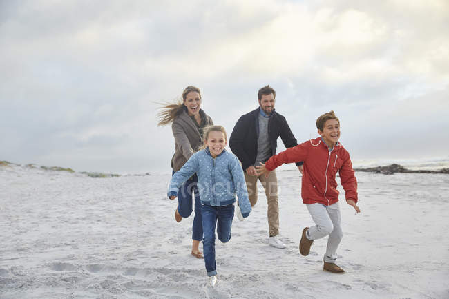 Famiglia giocosa che corre sulla spiaggia invernale — Foto stock