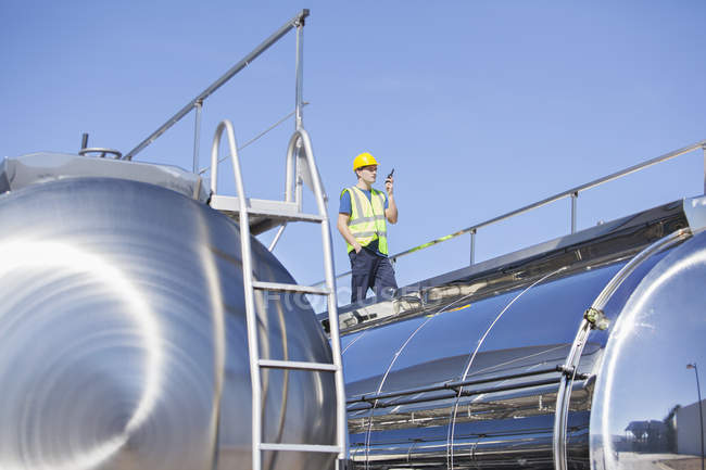 Worker using walkie-talkie on platform above stainless steel milk tanker — Stock Photo