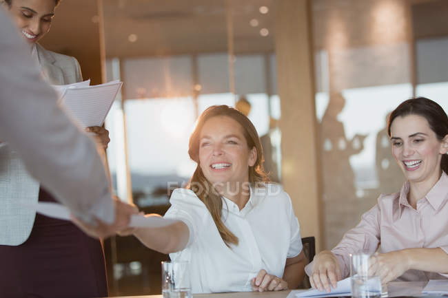 Une femme d'affaires souriante remet de la paperasse à un collègue lors d'une réunion en salle de conférence — Photo de stock