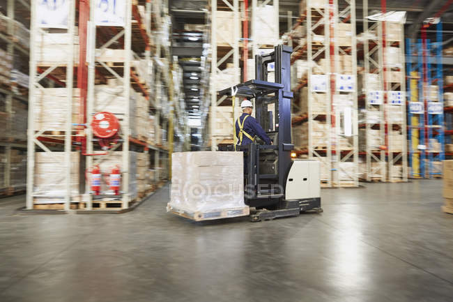 Travailleur opérant chariot élévateur mobile palette de boîtes dans l'entrepôt de distribution — Photo de stock