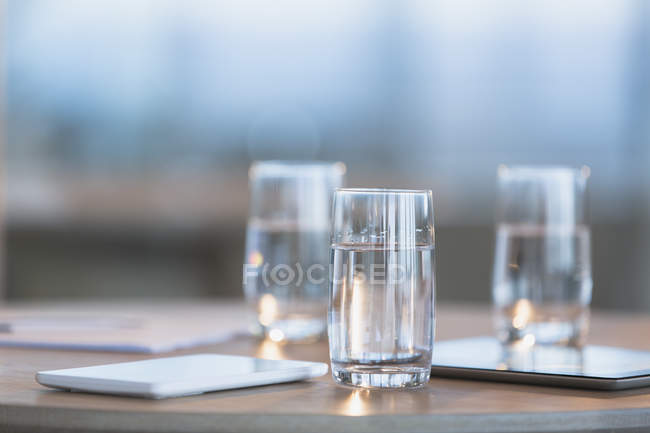 Agua en vasos junto a tabletas digitales en la mesa - foto de stock