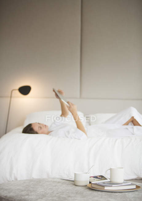 Жінка в халаті лежить на ліжку за допомогою цифрового планшета — стокове фото