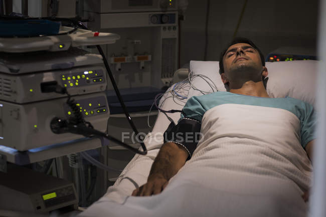 Patient lying in bed, attached to monitoring equipment in intensive care unit — Stock Photo