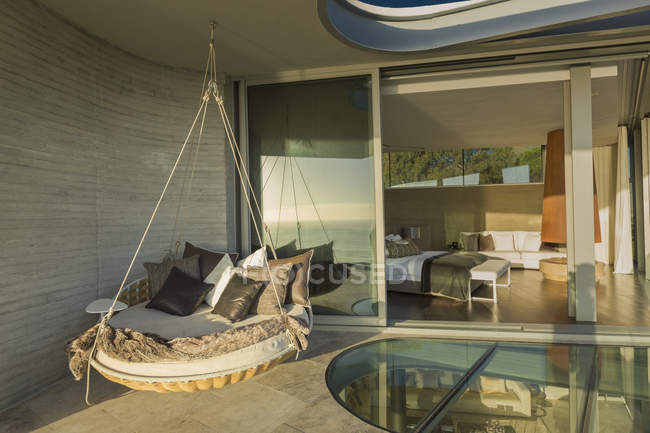 Cama de cojín colgante en soleado moderno patio escaparate casa de lujo - foto de stock