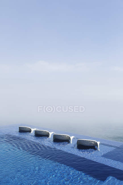 Lawn chairs in infinity pool overlooking ocean — Stock Photo