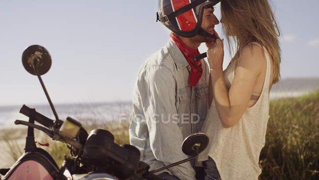 Liebevolles junges Paar auf Motorrad mit Strand im Hintergrund — Stockfoto