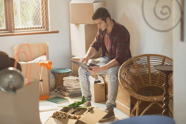 Hombre joven usando el ordenador portátil rodeado de cajas móviles en el apartamento - foto de stock