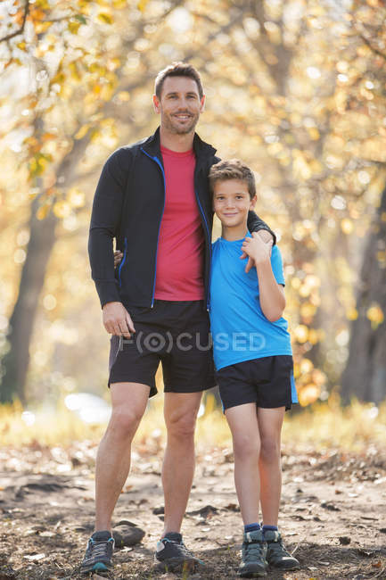Portrait smiling father and son in sportswear on path in woods — Stock Photo