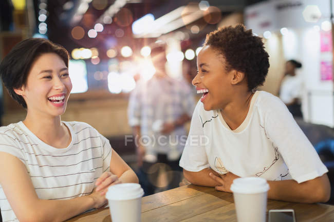 Смеющиеся молодые женщины пьют кофе в кафе — стоковое фото