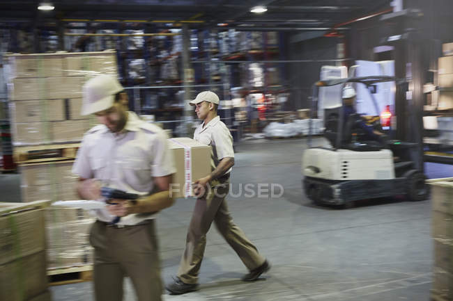 Trabajadores que transportan y mueven cajas con carretilla elevadora en el muelle de carga del almacén de distribución - foto de stock