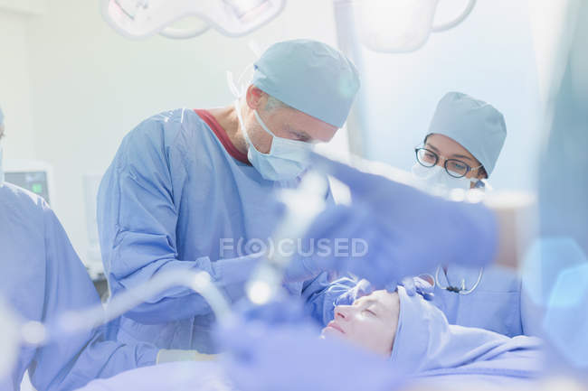 Cirujanos operando a una paciente femenina en quirófano - foto de stock