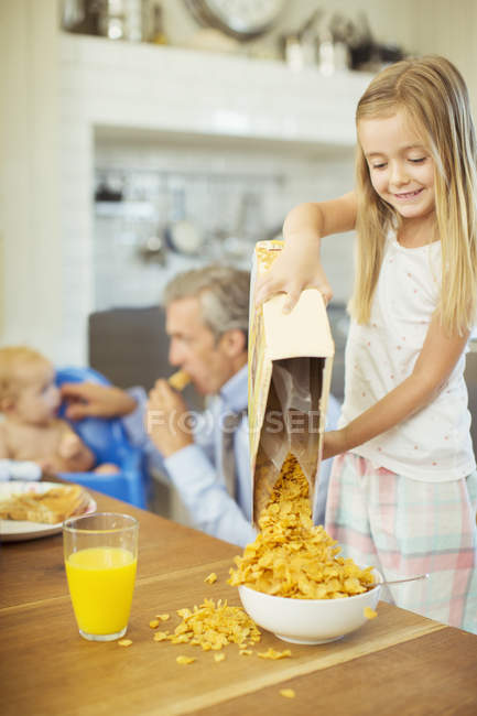 Девушка наливает хлопья в миску на стол для завтрака — стоковое фото