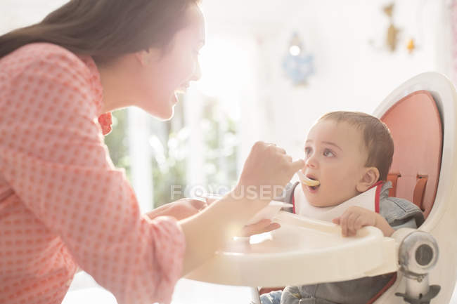 Mãe alimentando bebê menino em alta cadeira — Fotografia de Stock