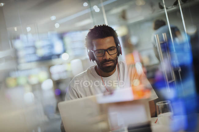 Hombre de negocios creativo enfocado con auriculares que trabajan en la computadora portátil en la oficina - foto de stock