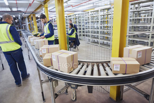 Travailleurs traitant des boîtes en carton sur bande transporteuse dans un entrepôt de distribution — Photo de stock