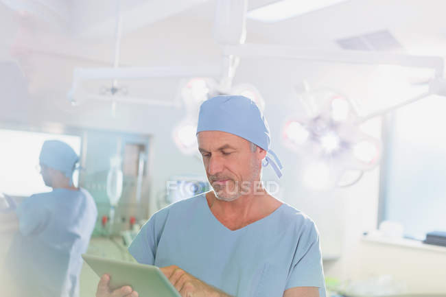 Літні чоловіки хірург використовуючи цифровий планшетний в операційний зал — стокове фото