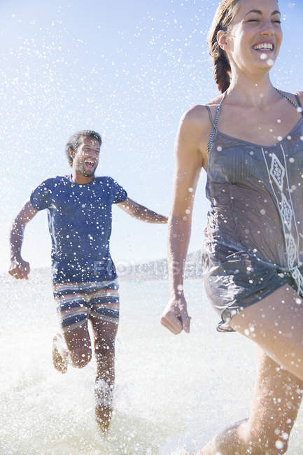 Casal espirrando na água na praia — Fotografia de Stock