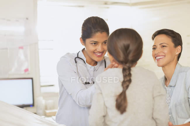 Pediatra femenina revisando las glándulas de los ganglios linfáticos del cuello de la paciente en la sala de examen - foto de stock