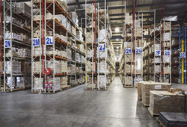 Mercancía apilada en estantes en pasillos etiquetados en almacén de distribución - foto de stock