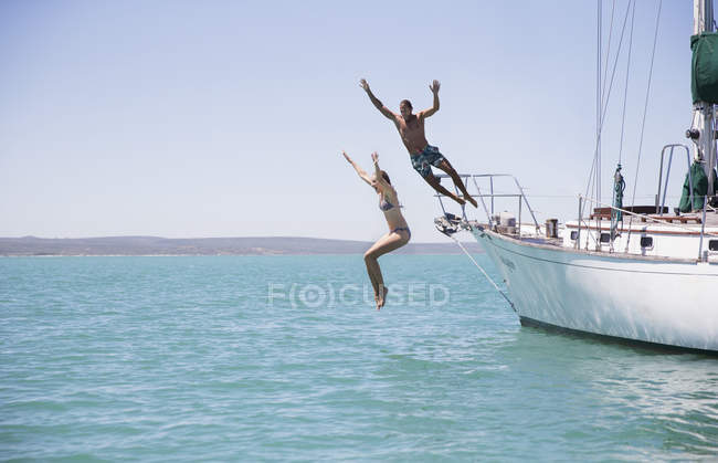 Couple jumping off boat into water — Stock Photo