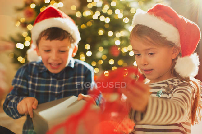 Hermano y hermana en los sombreros de Santa apertura de regalo de Navidad - foto de stock