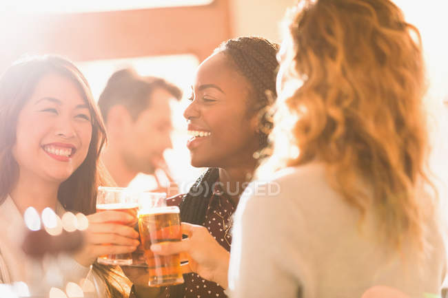 Улыбающиеся подруги пьют пивные бокалы в баре — стоковое фото