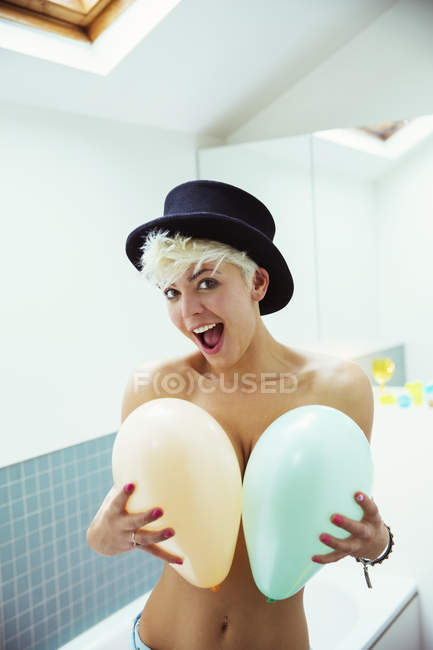 Woman in hat covering breasts with balloons — Stock Photo