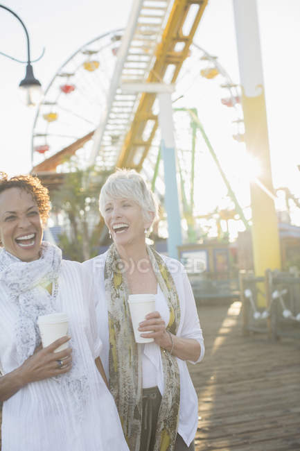 Женщины старшего возраста смеются и пьют кофе в парке развлечений — стоковое фото