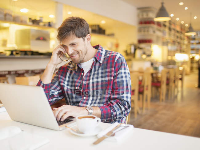 Happy young man using laptop in cafe — Stock Photo
