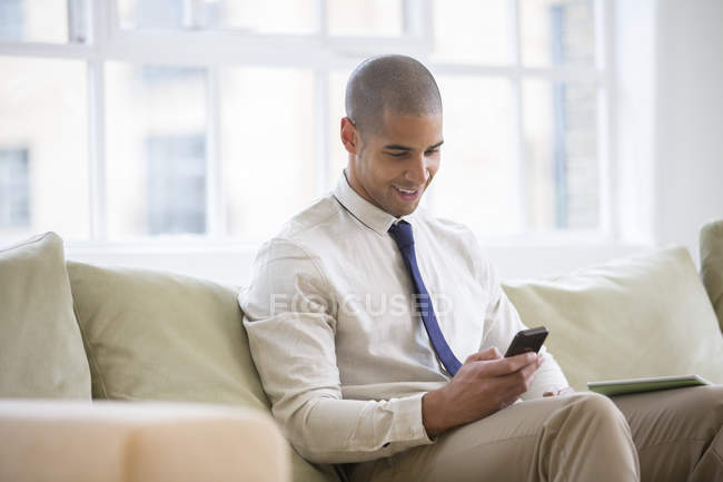 Бизнесмен, использующий сотовый телефон на диване дома — стоковое фото