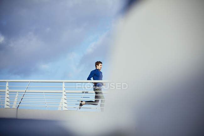 Male runner running on sunny footbridge — Stock Photo