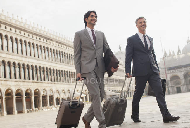 Uomini d'affari sorridenti che passeggiano con valigie per Piazza San Marco a Venezia — Foto stock