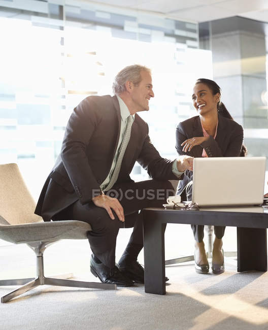 Smiling businessman and businesswoman using laptop in lobby at modern office — Stock Photo