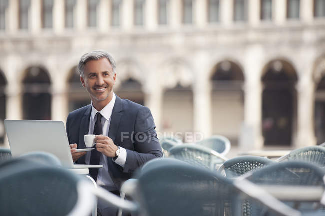 Lächelnder Geschäftsmann trinkt Espresso und benutzt Laptop im Straßencafé — Stockfoto